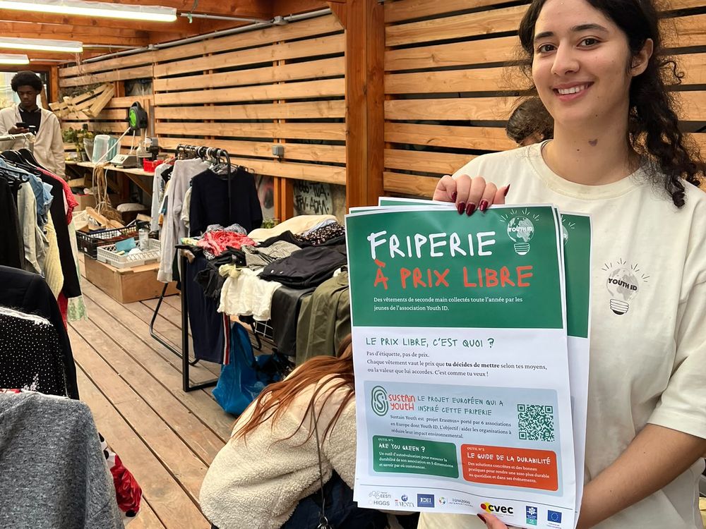 Bénévole présentant l'affiche de la friperie solidaire au Jardin des Traverses à Paris